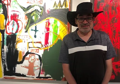 Paul Williams stands in front of a large colourfull painting.